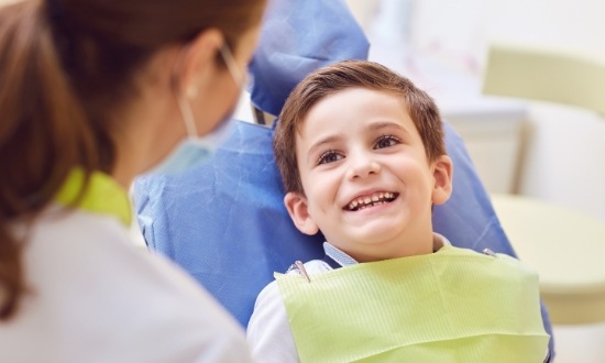 Young boy in dental chair smiling at his dentist