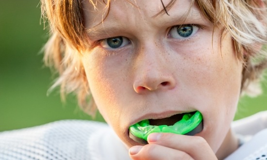 Young boy putting a green mouthguard into his mouth