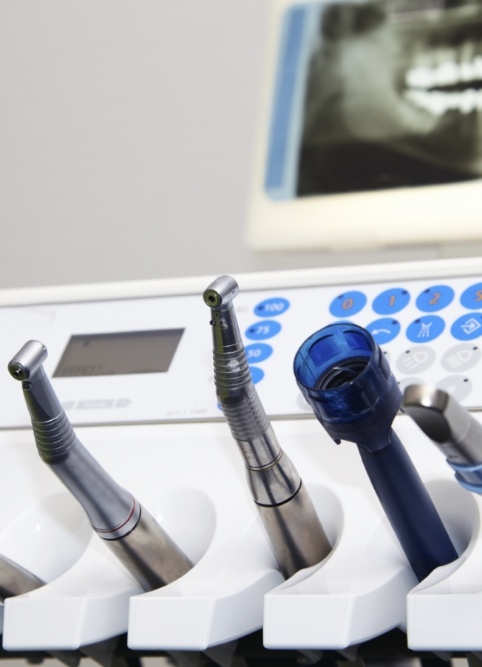 Row of dental instruments with screen showing x rays of teeth in background