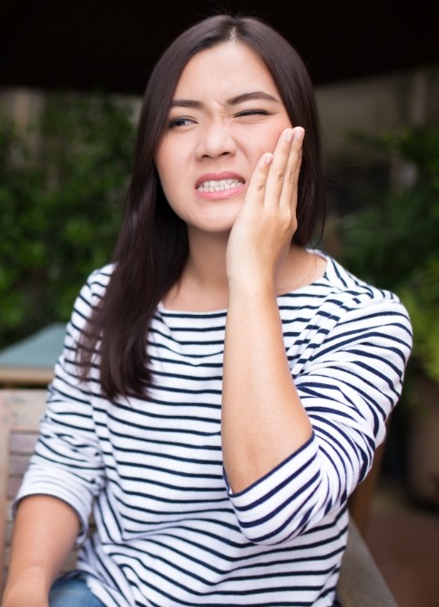 Woman wincing and holding her jaw in pain before emergency dentistry