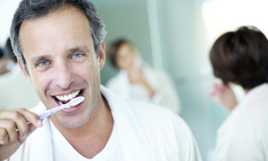 Man smiling while brushing his teeth