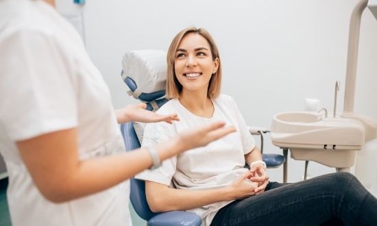 Woman in dental chair smiling while listening to her dentist