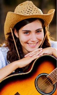 Smiling young woman in cowboy hat resting her hands on acoustic guitar