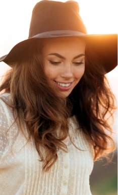 Woman in black wide brimmed hat grinning outdoors