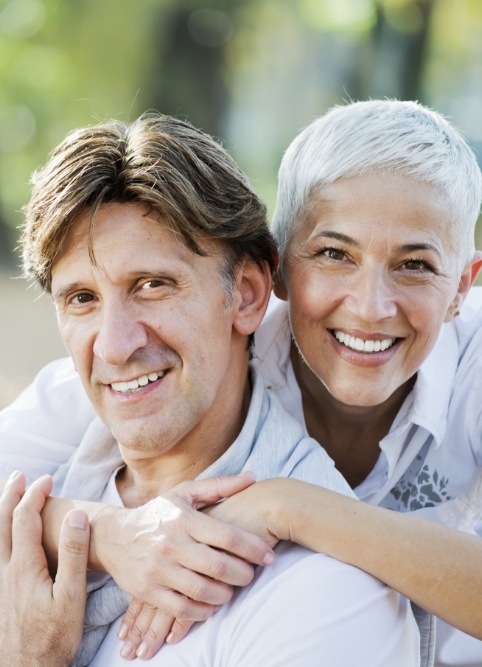 Older man and woman smiling outdoors after restorative dentistry treatment