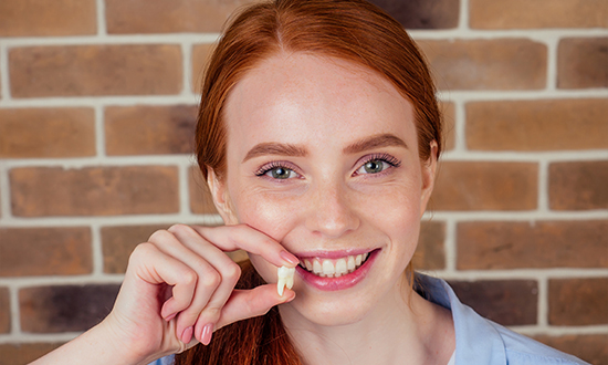 Smiling woman holding an extracted tooth