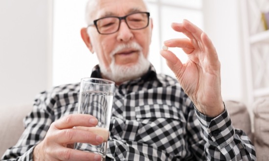 Senior man holding a pill and a glass of water