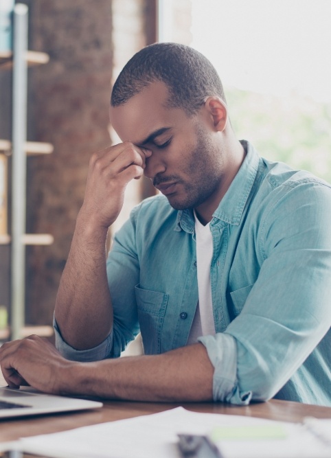 Man pinching the bridge of his nose while sitting at desk with laptop