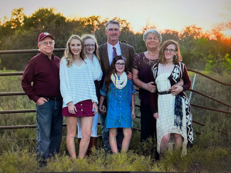 Three generations of a smiling family standing by a fence in grass